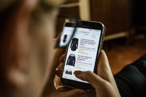 Person browsing clothing products on a smartphone, illustrating 24/7 accessibility and the impact of digital marketing on online shopping trends.